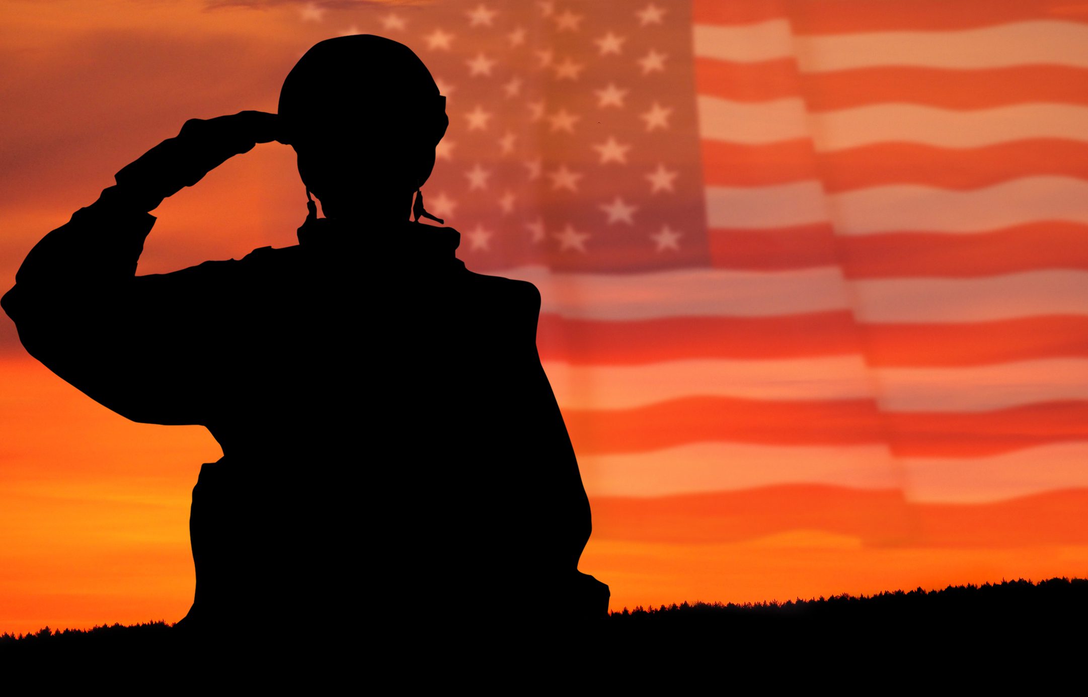 Silhouette of a soldier saluting with an American flag waving behind him