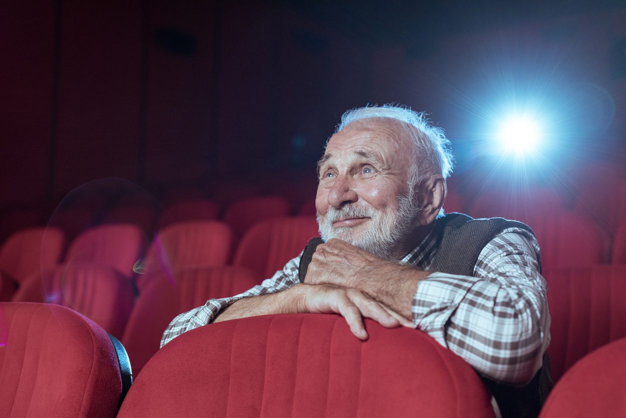 Smiling older man watching film in darkened theater.